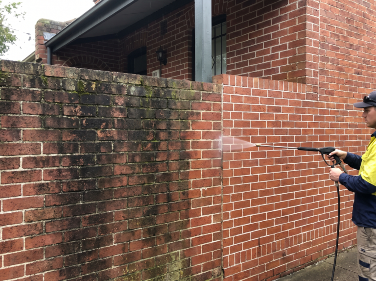 Heritage red brick wall with tuck pointing being gently washed, half grimy half restored