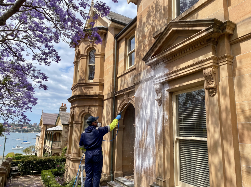Technician soft washing a Victorian harbourside home facade in Darling Point
