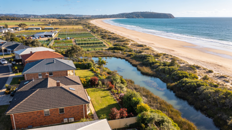 Flat coastal plain suburb with low brick homes, a wide beach beyond and wetland inland