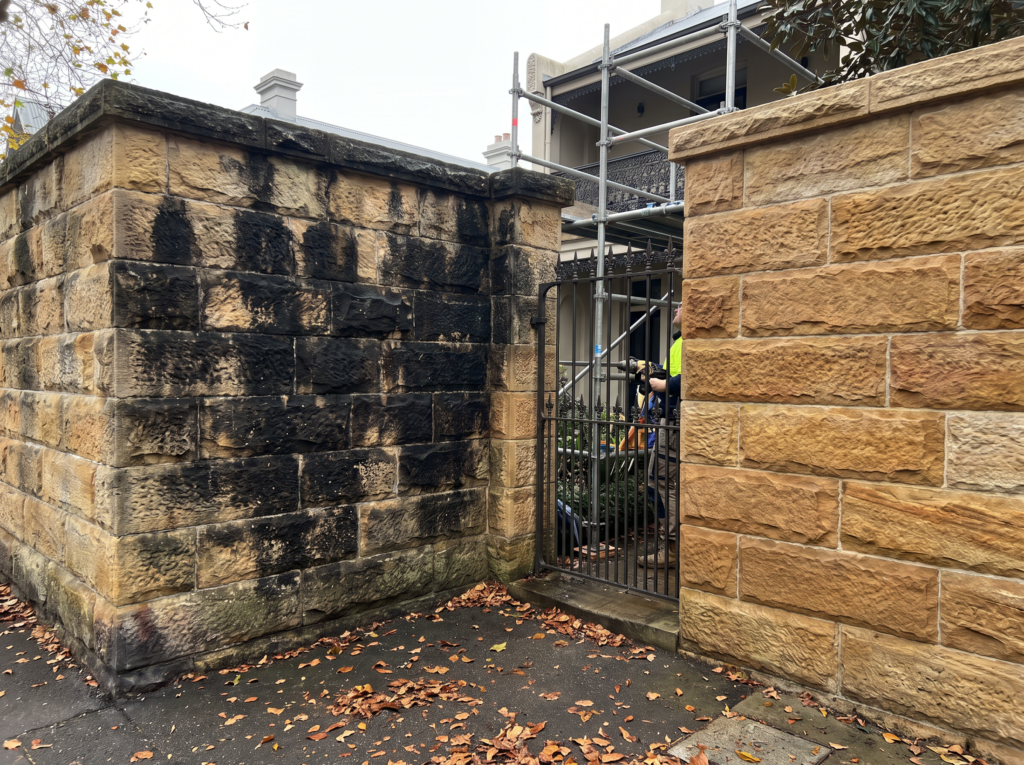 Golden sandstone boundary wall in Woollahra half restored from black biological crust
