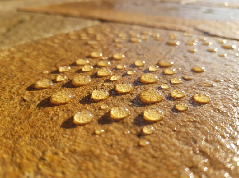 Close-up of water beading on freshly sealed golden sandstone paving