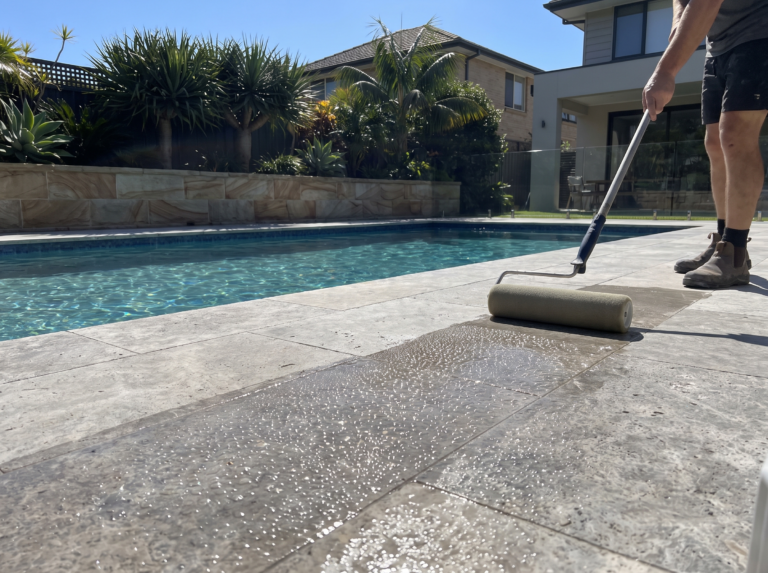 Silver travertine pool surround being sealed with water beading on the finished half