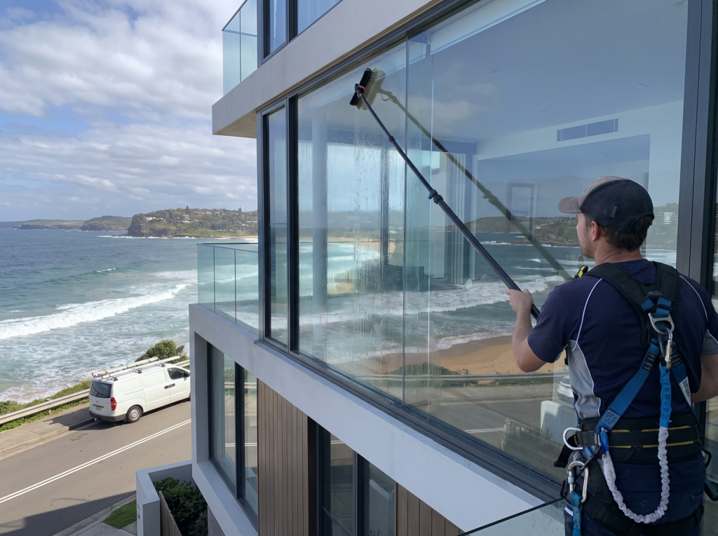 Water-fed pole cleaning full-height ocean-facing glass on a Northern Beaches home