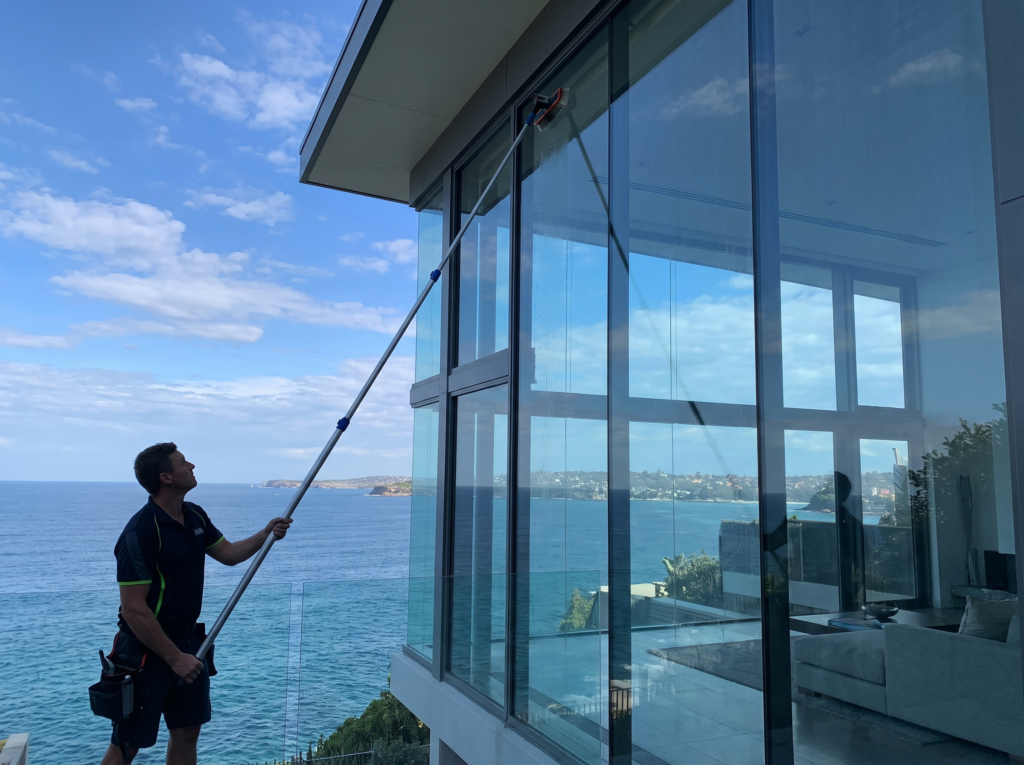 Window cleaner using a water-fed pole on tall ocean-view glazing of a modern Vaucluse home